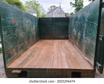 An Empty Open Dumpster Sitting In A Driveway. The Dumpster's Walls Are Covered In Scratches And Grooves. 