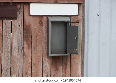 Empty Open Gray Metal Mailbox On A Brown Fence Wall And Wooden Boards In The Street