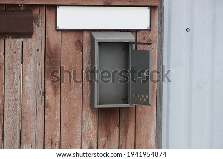 empty open gray metal mailbox on a brown fence wall and wooden boards in the street