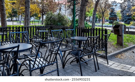 Empty outdoor cafe chairs and tables under autumn trees highlight social distancing challenges during fall gatherings - Powered by Shutterstock