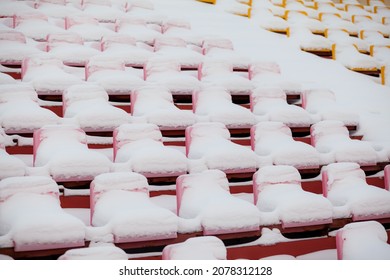 Empty outdoor football soccer stadium seats covered with snow in winter, light snowfall. Plastic seats in a row at the stadium are covered with snow snow. - Powered by Shutterstock