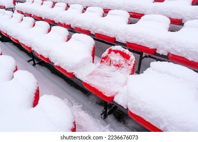 Empty outdoor football soccer stadium seats covered with snow in winter. Red plastic seats in a row at the stadium are covered with snow. - Powered by Shutterstock