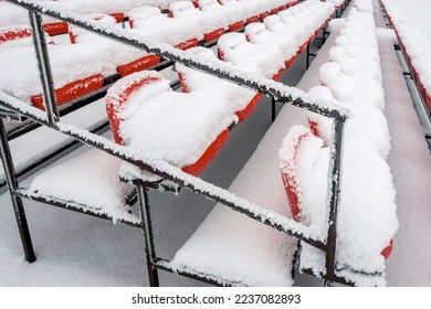 Empty outdoor football soccer stadium seats covered with snow in winter. Red plastic seats in a row at the stadium are covered with snow. - Powered by Shutterstock