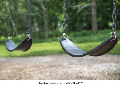 An empty pair of swings hang at the playground. No children are playing on the swing set, which is not moving.  The swings are clean and well maintained.  Back to School. Recess equipment. Outdoors. 