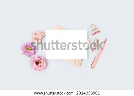 Empty paper card mockup, stationery and eustoma flowers on a blue pastel background. Feminine workspace with copyspace. Springtime concept.
