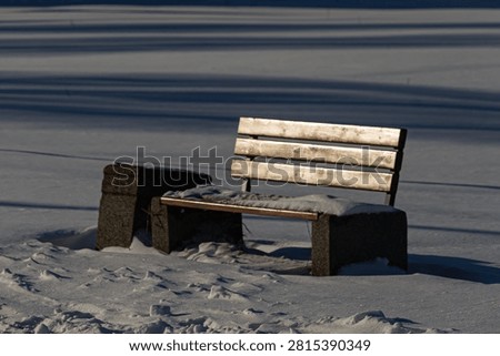 Empty park bench standing in deep snow with long shadows on a cold winter day