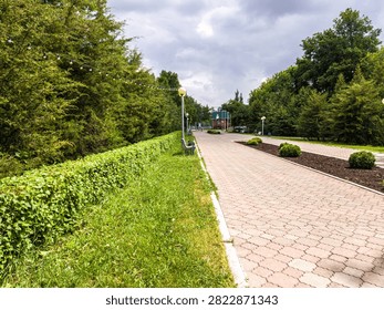 Empty park pathway lined with green hedges and trees.