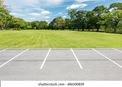 Empty Parking Lot Against Green Lawn In City Park 