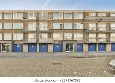 an empty parking area in front of a multi - storey apartment building with blue doors and bales on the windows