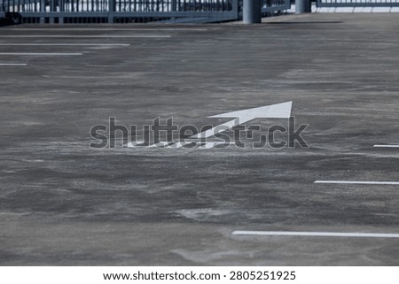 Empty parking bays with a white directional arrow on the concrete deck of an open car park.