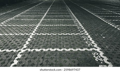 An empty parking lot with hexagonal paving blocks, partially overgrown with grass, creating a textured and slightly abandoned appearance.