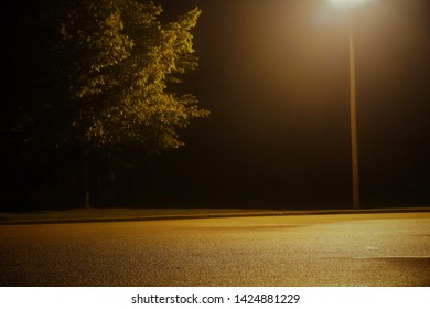 An Empty Parking Lot At Night, Lit By A Single Street Light.