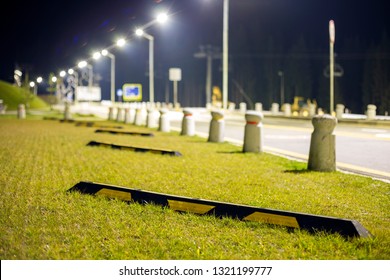 Empty Parking Lot On Green Lawn Brightly Illuminated By Street Lamps Along Road On Dark Night Sky Copy Space Background.