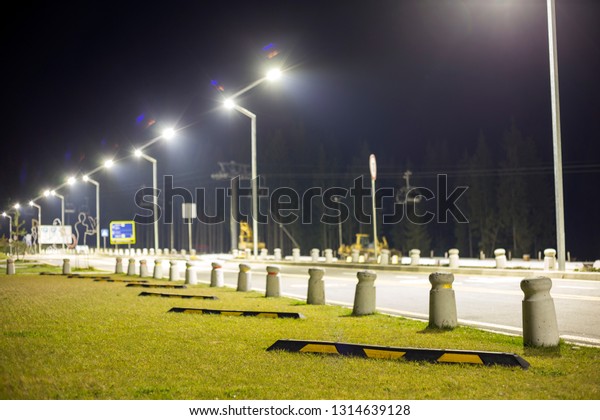 Empty\
parking lot on green lawn brightly illuminated by street lamps\
along road on dark night sky copy space\
background.