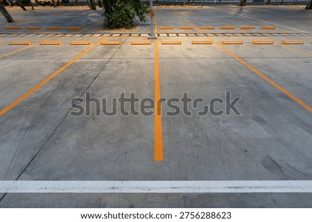 Empty parking space with orange lines on a concrete surface showing a clean layout and organized structure for vehicle positioning.
