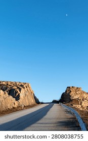 Empty paved road running through rocky hills under a clear blue sky.