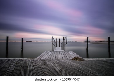 An empty peaceful dock within a marina as clouds streak across the sky. Still water, serene and calm scene
