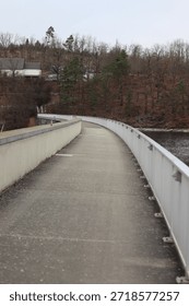 Empty pedestrian and bicycle path over a dam leading into the distance, surrounded by autumn trees. Concept of journey, direction, infrastructure, transition and calm movement.