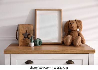 Empty Photo Frame Near Cute Toy Bunny And Decor On Dresser, Space For Text. Baby Room Interior Element