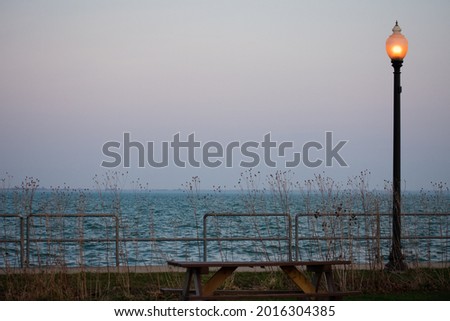 An empty picnic table to the left of an oil lamp overlooking lake st clair. Taken at Walter Mary Burke Park  in New Baltimore, MI. The dark rain clouds in the sky contrast to the bright blue water. 