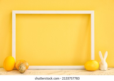 Empty picture frame, Easter eggs and decorative rabbit on table against color background, closeup