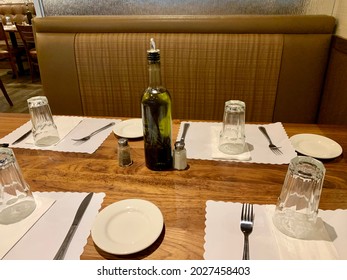 An Empty Place Setting Waiting For Patrons To Enter The Small Business For A Meal. The Restaurant Set This Table For Four With Plates, Place Mats, Cups, Condiments, And Fresh Olive Oil.