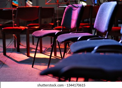 Empty Places For Orchestra On Stage. The Chairs Are Lit By Red And Blue Light Floodlights.