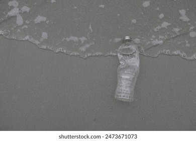 Empty plastic bottle washed up on shore with ocean waves. Environmental pollution and marine debris concept.
