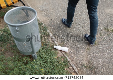 An empty of plastic drinking bottle littering on the road floor, near the rubbish bin. Concept of environmental protection.
