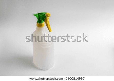 Empty plastic trigger spray bottle isolated on white background, reusable household cleaning container with green and yellow nozzle, studio product photo with copy space.