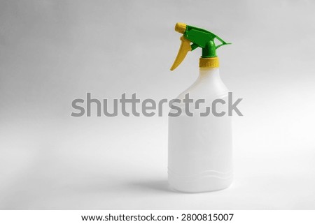 Empty plastic trigger spray bottle isolated on white background, reusable household cleaning container with green and yellow nozzle, studio product photo with copy space.