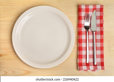 Empty plate with cutlery on red checkered napkin on wooden background. - Powered by Shutterstock