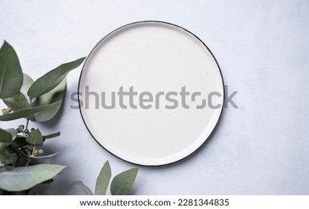 An empty plate with eucalyptus branches on a light background. Festive table setting. Top view and place to copy.