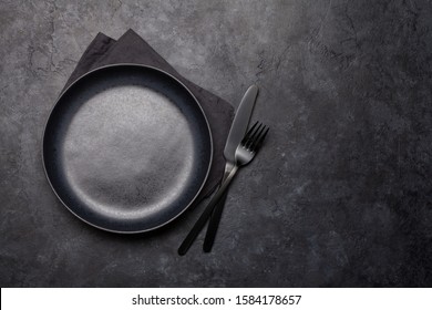 Empty plate, fork and knife. Black kitchen utensils set on stone table. Top view flat lay with copy space