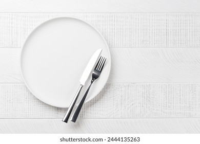 Empty plate, fork and knife on wooden table, overhead view with copy space