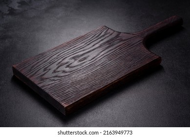 An empty plate with a knife, fork or spoon with a wooden cutting board on a dark concrete background. Preparation of appliances and ingredients for home cooking - Powered by Shutterstock