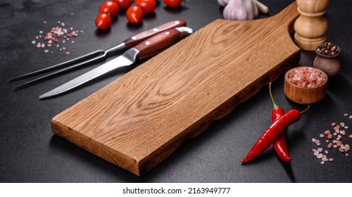 An empty plate with a knife, fork or spoon with a wooden cutting board on a dark concrete background. Preparation of appliances and ingredients for home cooking - Powered by Shutterstock