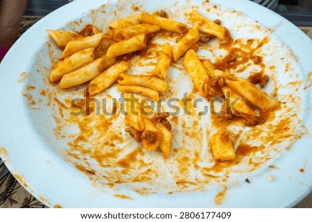 Empty plate with leftover macaroni pasta highlighting food waste, overconsumption, and imperfect messy dining experiences indoors.