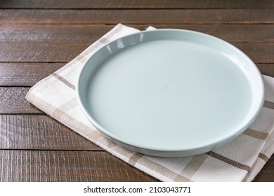 Empty plate on napkin on wooden table over grunge blue background. Clear ceramic dish for cafe on wood surface. Food background for menu and recipe or restaurant. Table setting