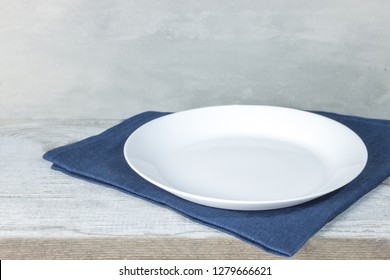 Empty plate on tablecloth on wooden table over grunge background. Table setting. Circle white dish.