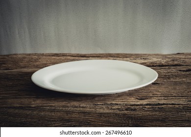 Empty Plate on wooden tabletop against grunge wall. vintage tone