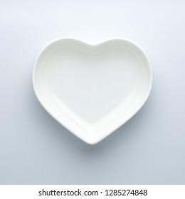 Empty plate in the shape of a heart on a white background in the center of the frame. Minimalism. Copy space. Modern ceramic glossy dishes. Concept of Valentine's Day or wedding romantic theme. Square