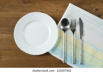 Empty plate and silverware set on wooden table