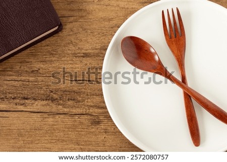 Empty plate with spoon and fork and holy bible book on wooden background. Top view. Christian fasting and spiritual food, biblical concept.