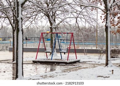 empty playground, bright swing set for children covered with snow on winter background, no people. Cold frosty weather, abandoned city