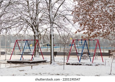 Empty Playground, Bright Swing Set For Children Covered With Snow On Winter Background, No People. Cold Frosty Weather, Abandoned City