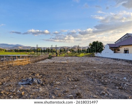 An empty plot of land, ready for construction, surrounded by lush green rice fields, offering a peaceful rural setting