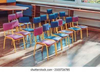 Empty Preschool Classroom With Multi Colored Chairs Standing In Rows Lighting With Bright Light Through Window Glass. Education And Back To School Concept.