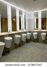 Empty Public Bathroom With White Sinks And Wide Wall Mirror, And Toilets