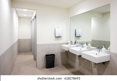 Empty Public Bathroom With White Sinks And Wide Wall Mirror, Air Hand Drier And Black Recycle Bin